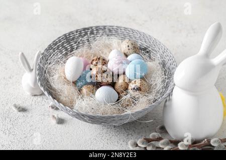 Bowl of Easter eggs and ceramic bunnies on light background Stock Photo