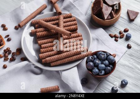 Plate with delicious chocolate wafer rolls and blueberries on grey wooden background Stock Photo