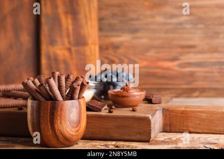 Bowl with delicious chocolate wafer rolls on brown wooden table Stock Photo