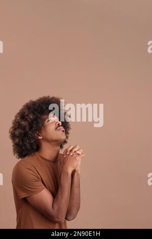 African man looking up while praying with folded hands Stock Photo