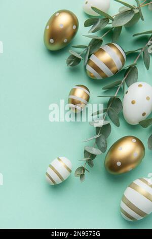 Easter eggs painted in gold and eucalyptus branches on a soft green background. Festive background Stock Photo