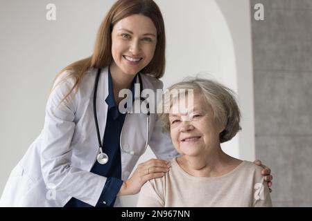 Happy pretty female doctor with stethoscope embracing older patient Stock Photo
