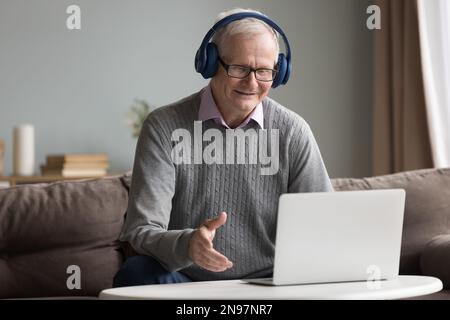 Cheerful older man in wireless headphones talking on video call Stock Photo