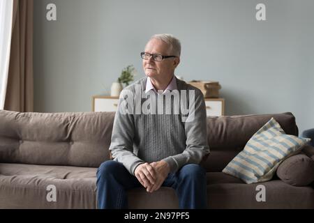 Serious pensive senior pensioner man sitting on home couch Stock Photo