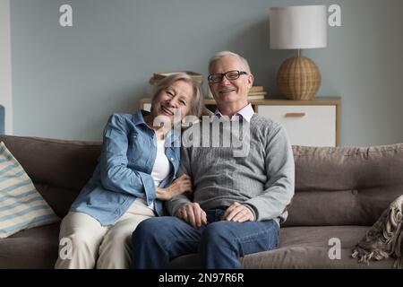 Happy elderly married couple posing at home, sitting on sofa Stock Photo