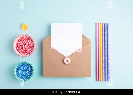 Empty card in kraft envelope and sweet birthday decorations on pastel blue background. Flatlay, knolling composition, copy space. Stock Photo