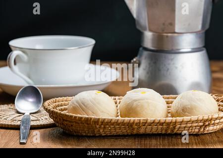 View of homemade chinese pastry or moon cake filled with sweet mung bean paste and salted egg yolk in bamboo tray with white ceramic cup of coffee Stock Photo