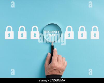 To find or discover a security gap or breach in the system. Hand holds magnifying glass focusing on the word security gap next to padlock icons. Stock Photo
