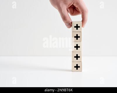 Added value or increasing benefits concept. Progress and profit to benefit growth and development in business. Hand places cube with plus symbol on to Stock Photo