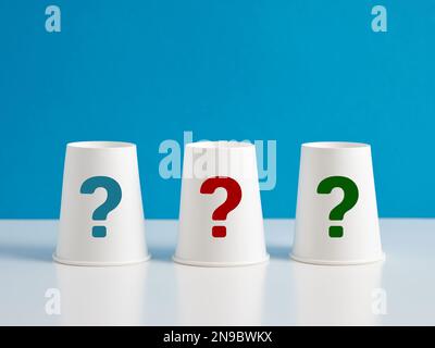 Problem, solution, uncertainty, confusion and choice. Three paper cups with question mark symbols on blue background. Stock Photo