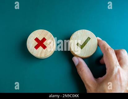 Right and wrong. Close-up green check mark and red X mark icon on round wooden button, chosen green check mark by business's hand. Picking correct sig Stock Photo