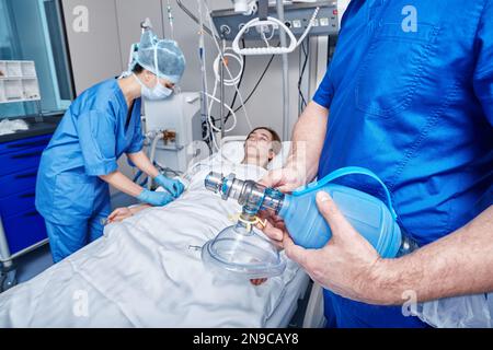 doctor holding oxygen mask near unconscious patient in ICU while cardiopulmonary resuscitation. Intensive care unit Stock Photo