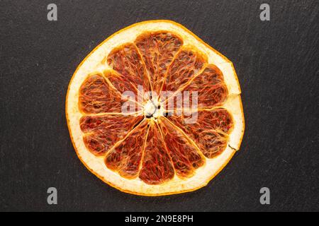 One dry slice of grapefruit on slate stone, macro, top view. Stock Photo