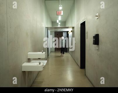 Eerie photo of a generic concrete bathroom hallway with drinking fountains and older woman walking out the door. Stock Photo