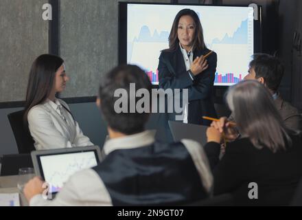 Modern Corporate Meeting. asian Businesswoman  Giving Speech During Seminar With Coworkers In Office, Showing Growth Chart On Screen Monitor Standing Stock Photo