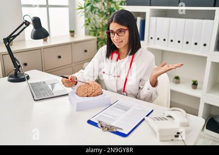 Young latin woman wearing doctor uniform pointing to brain at clinic Stock Photo