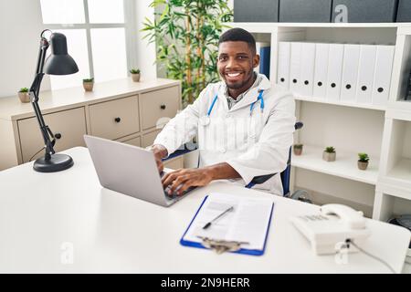 Young african american man wearing doctor uniform sitting on wheelchair working at clinic Stock Photo
