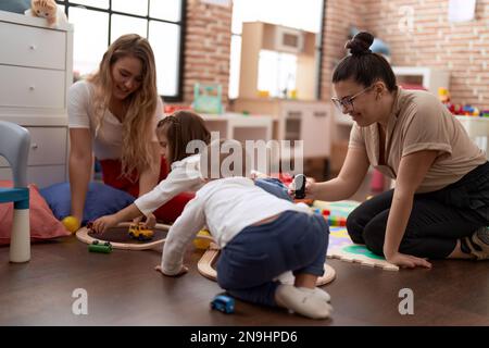 Teachers with boy and girl playing with cars toy sitting on floor at kindergarten Stock Photo