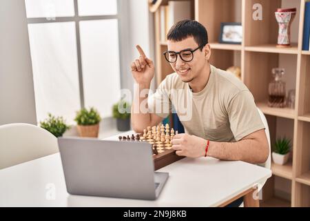 Young arab man playing chess online smiling happy pointing with hand and finger to the side Stock Photo