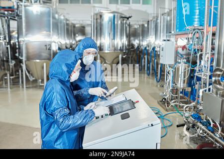 Side view portrait of two workers operating equipment at factory and using control panel Stock Photo