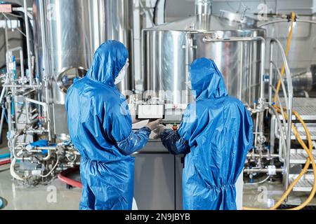Back view of two workers using control panel while operating equipment at chemical factory Stock Photo