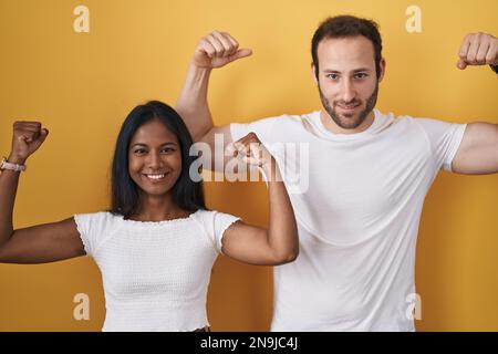 Interracial couple standing over yellow background showing arms muscles smiling proud. fitness concept. Stock Photo