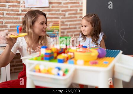 Teacher and toddler playing with construction blocks sitting on table at kindergarten Stock Photo