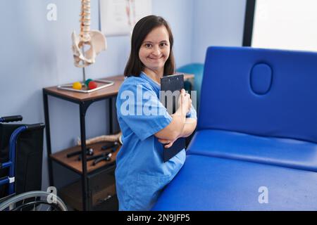 Down syndrome woman wearing physiotherapy uniform holding clipboard at physiotherapist clinic Stock Photo