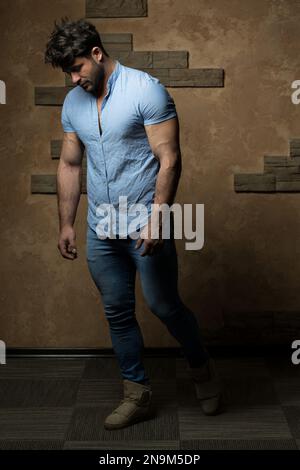 A vertical Portrait of a Handsome Young Man in Jeans Clothes Standing Against a Brick Wall Stock Photo