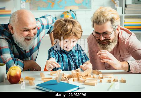Grandfather father and cute little son having fun at home. Parenting childhood values weekend. Male multi generation portrait Playing Jenga. Stock Photo