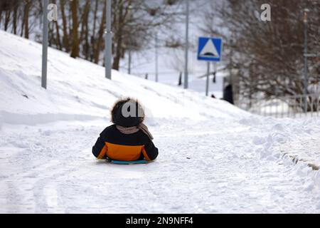 Child riding on sledge by the snowy road, little boy during tubing in winter park Stock Photo