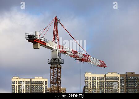 Tower crane above new buildings on background of blue sky with clouds. Housing construction, apartment blocks in city Stock Photo