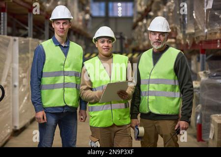 Front view portrait of group of workers wearing hardhats in warehouse and looking at camera Stock Photo