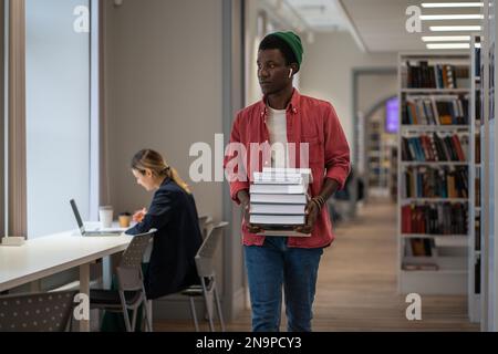 Student with huge stack of educational books goes to library workplace to prepare for entrance exams Stock Photo