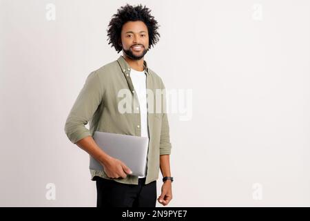 Attractive 30s African American man wearing green casual shirt standing isolated on white, carrying laptop computer, smiling, male office employee, student, copy space Stock Photo