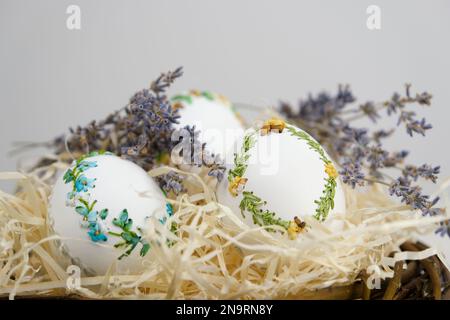 easter holiday in a nest white eggs with a pattern embroidery ribbons on eggshell lavender flowers decoration close-up easter holiday succeeded shavings for packaging embroidery ribbons on eggshells Stock Photo