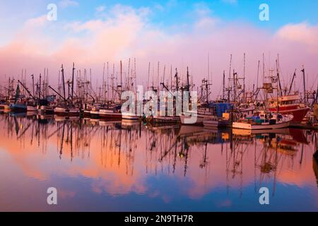 Sunrise light through morning fog and fishing boats reflected in mirror image into the water in Newport harbour on the Oregon Coast Stock Photo