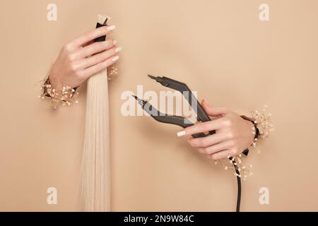 Hands with flowers hold strands of hair for extensions on a beige background. Stock Photo