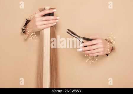 Hands with flowers hold strands of hair for extensions on a beige background. Stock Photo