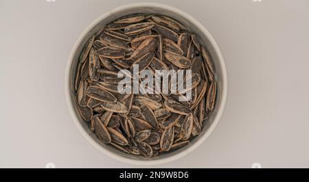 Top view of salted and roasted sunflower seeds in a white bowl. Isolated on white. Close up Stock Photo