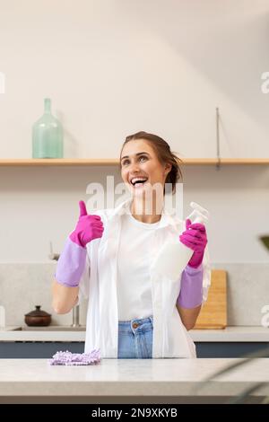 Attractive housewife holds a spray bottle with cleaning agent in her hand and shows a thumbs up.  Stock Photo