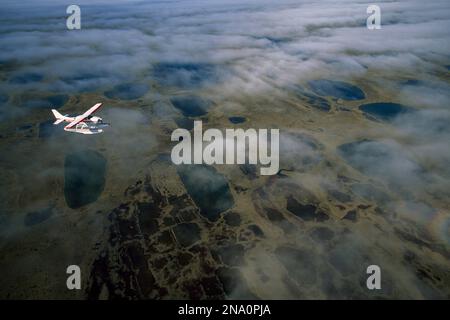 Seaplane over clouds and the tundra of Alaska's North Slope; North Slope, Alaska, United States of America Stock Photo