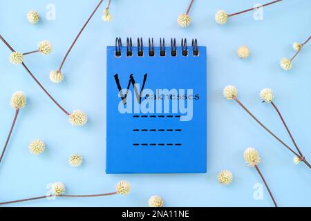 List of personal weaknesses written on blue notepad. Personality development beautiful flat lay composition. Stock Photo