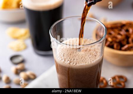 Pouring dark stout beer in a tall glass, beer and snacks on the table Stock Photo