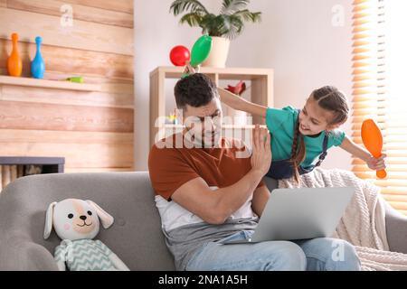 Cute child disturbing stressed man in living room. Working from home during quarantine Stock Photo