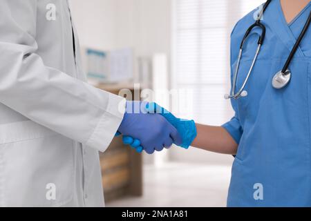 Doctors in medical gloves giving handshake at hospital, closeup Stock Photo