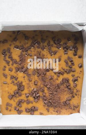 Blondie batter with chocolate chips in a parchment lined square baking tin, cake batter in a 10 inch baking pan Stock Photo