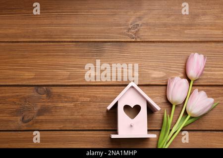 Beautiful bird house with heart shaped hole and tulips on wooden background, space for text. Spring flat lay composition Stock Photo