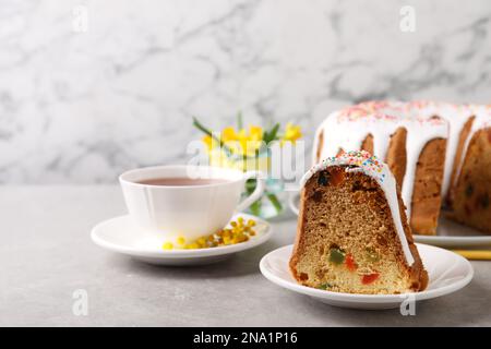 Piece of glazed Easter cake with sprinkles and tea on grey table, space for text Stock Photo