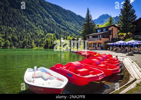 Red boats lined up at Champex Lake with an outdoor cafe under blue sky; Champex, Valais, Switzerland Stock Photo